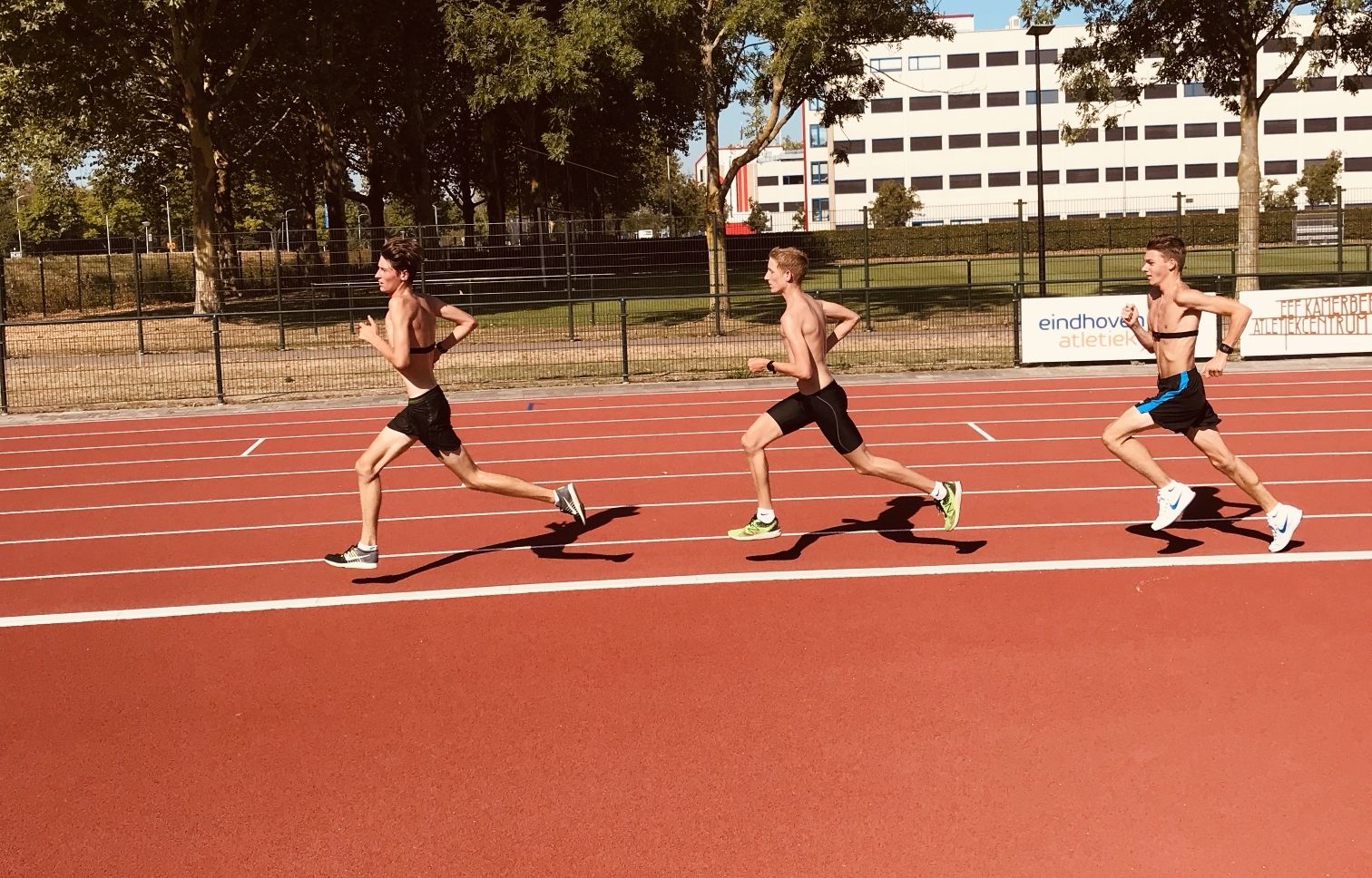 Drie lopers in een treintje op de atletiekbaan
